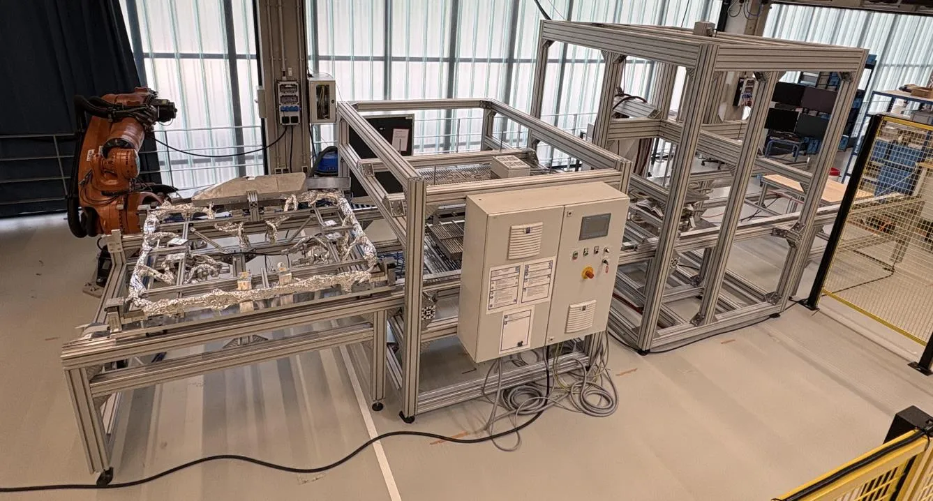 The stamp-forming line with gripper frame, infrared oven and press on a linear axis, with an industrial robot in the background.